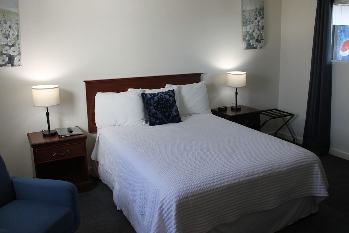 A hotel room with a large bed, two bedside tables, a chair, and a window with curtains.