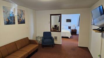 Een hotelkamer met een bruine bank, een blauwe fauteuil, een bed, een televisie en abstracte kunst aan de muren.