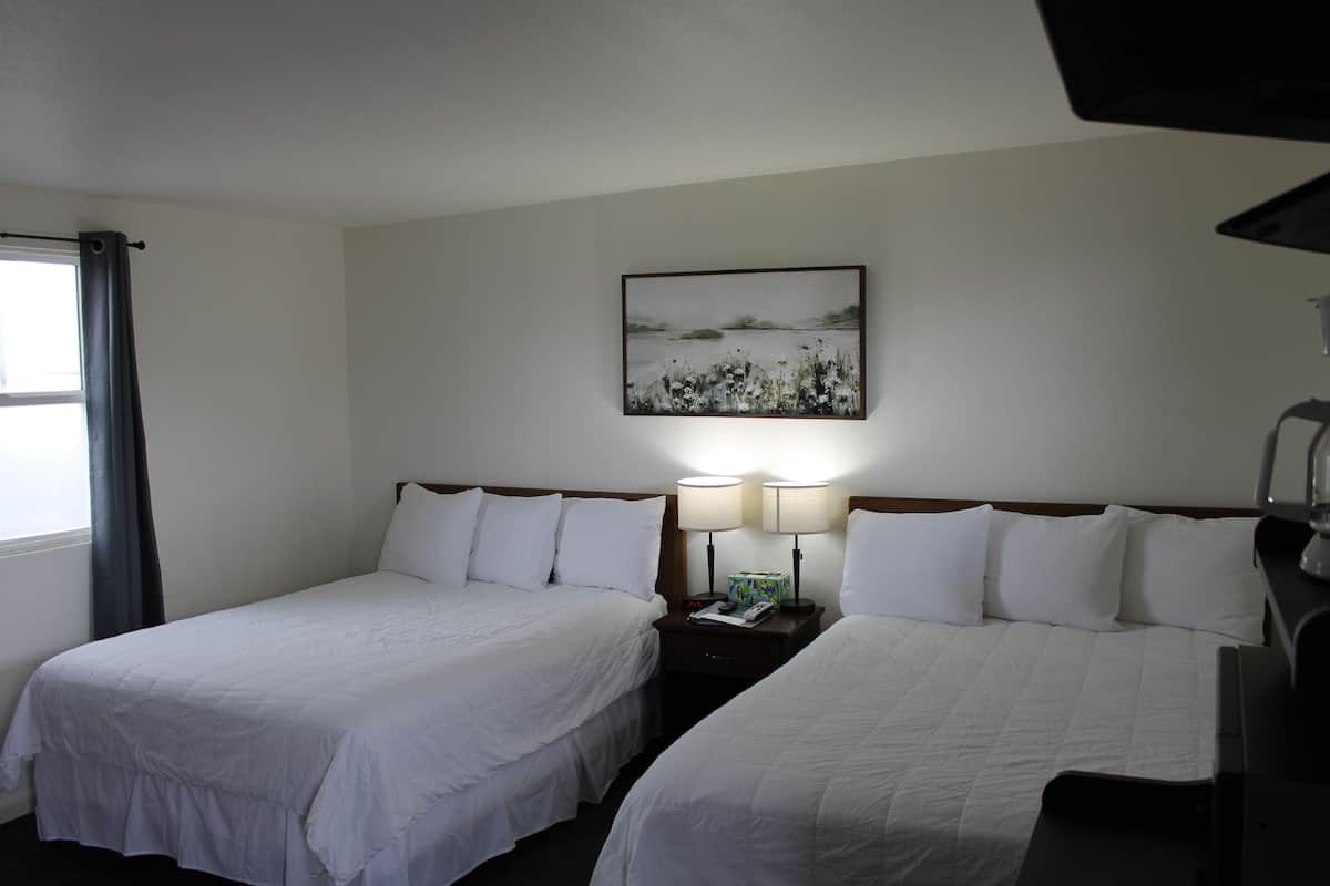 A hotel room with two single beds, a nightstand with lamps, a painting on the wall, and a window with curtains.