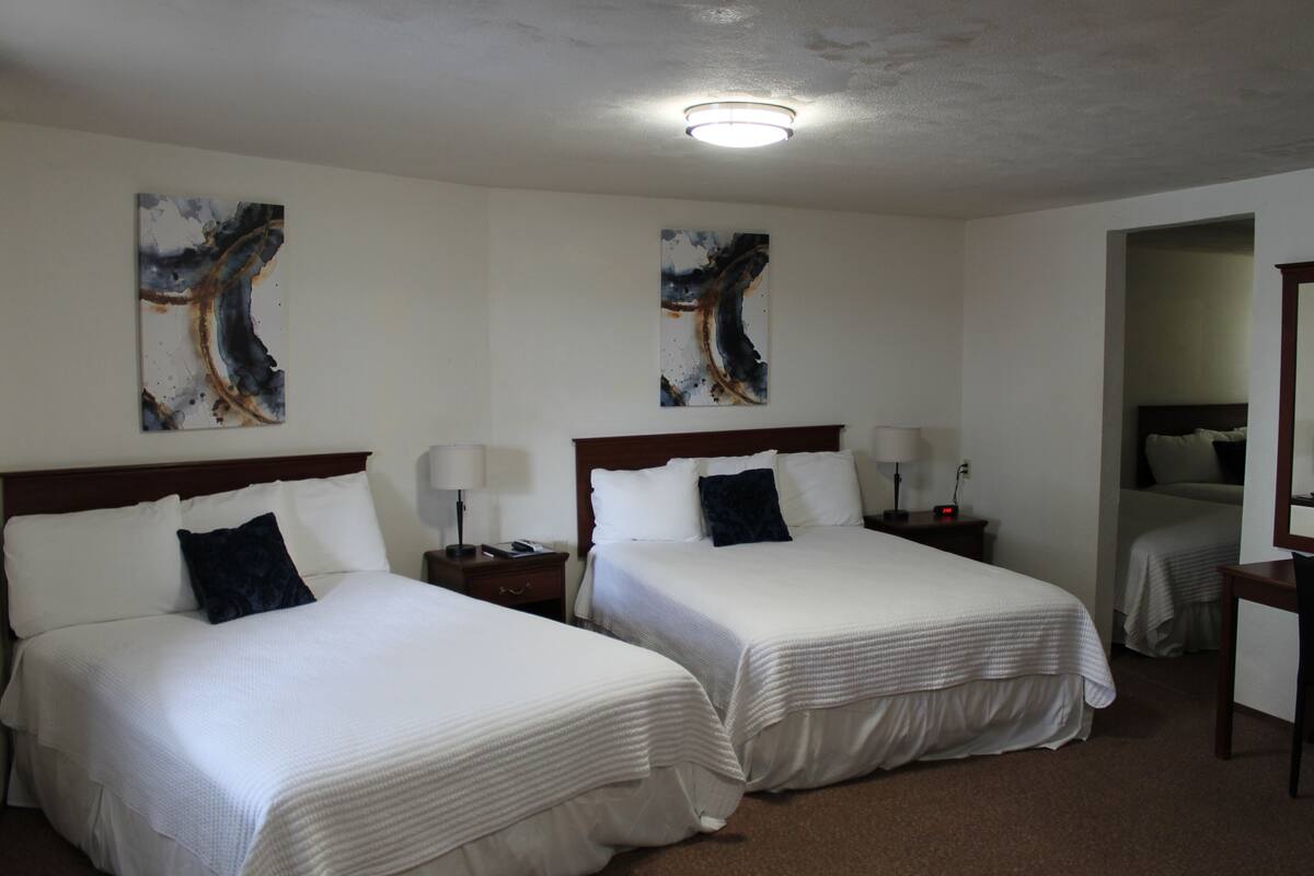 A hotel room with two beds, each with a nightstand, a lamp, and abstract artwork on the wall.