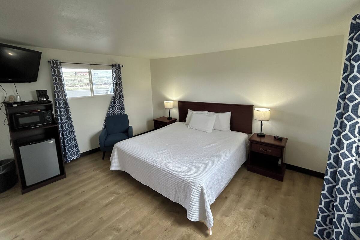 A hotel room with a bed, bedside lamps, a TV, a coffee maker, and a small refrigerator.