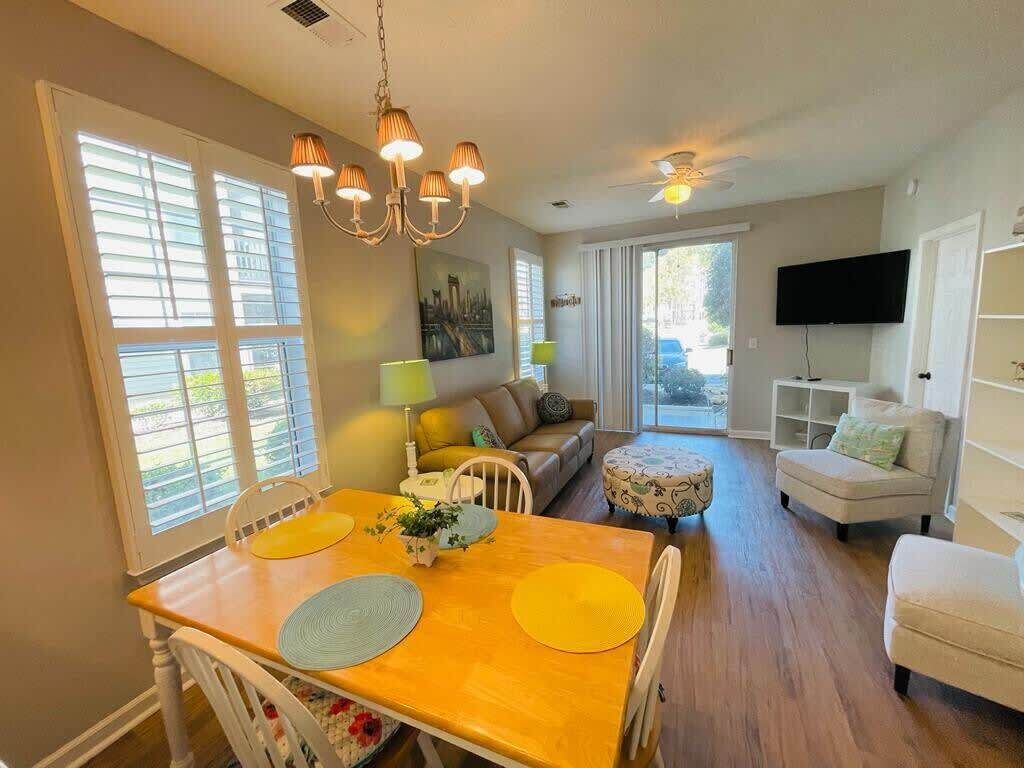 A dining area with a wooden table and chairs, a chandelier, and a sofa in the background.
