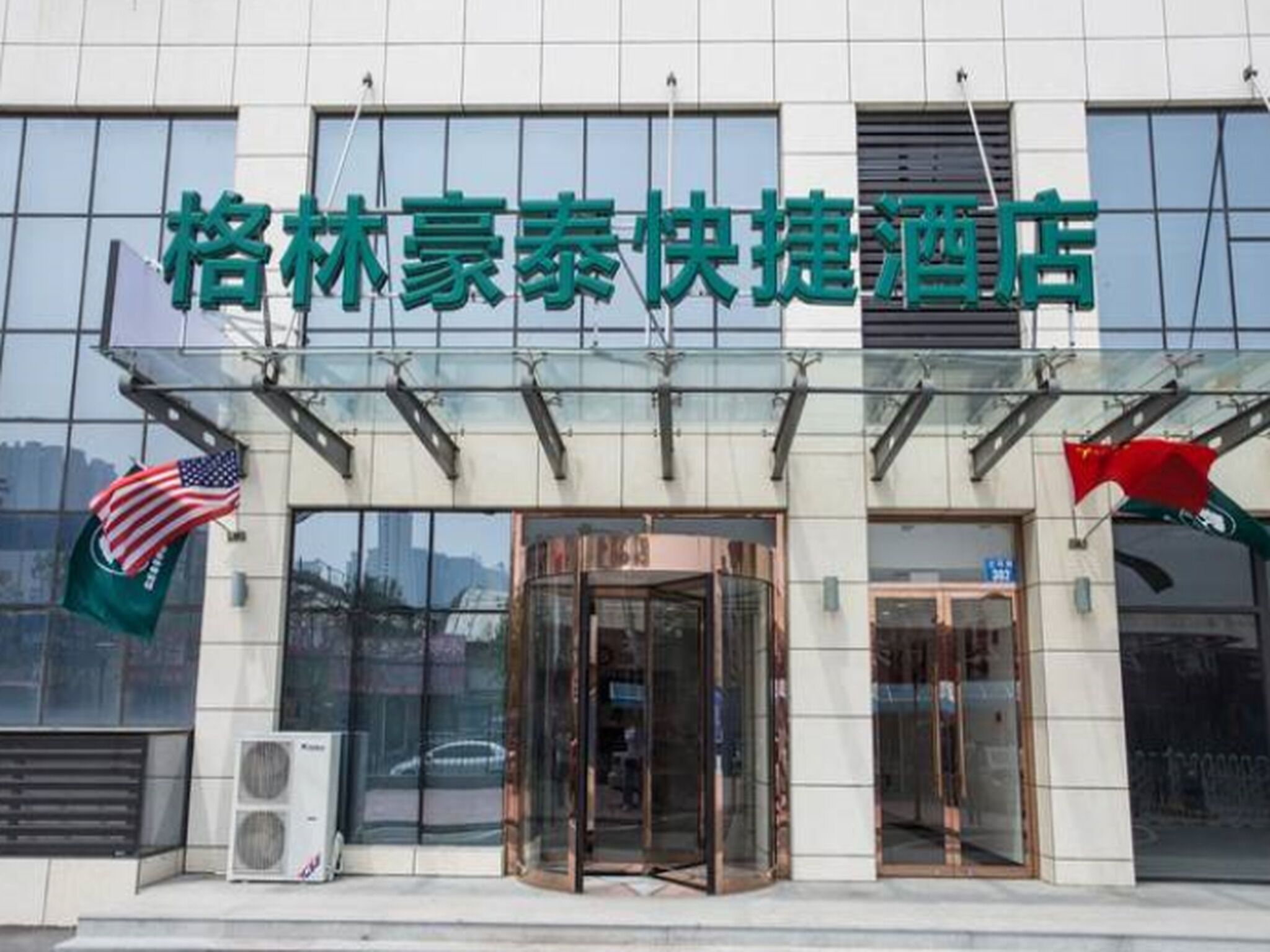 A hotel entrance with a glass facade, American and Chinese flags, and a revolving door.