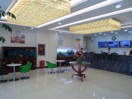 A hotel lobby with a reception desk, green chairs, a round table, and a large aquarium.