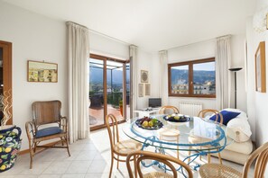 A dining area with a glass table, wicker chairs, and a view of the city through large windows. - Maison Miramar  (Sorrento)