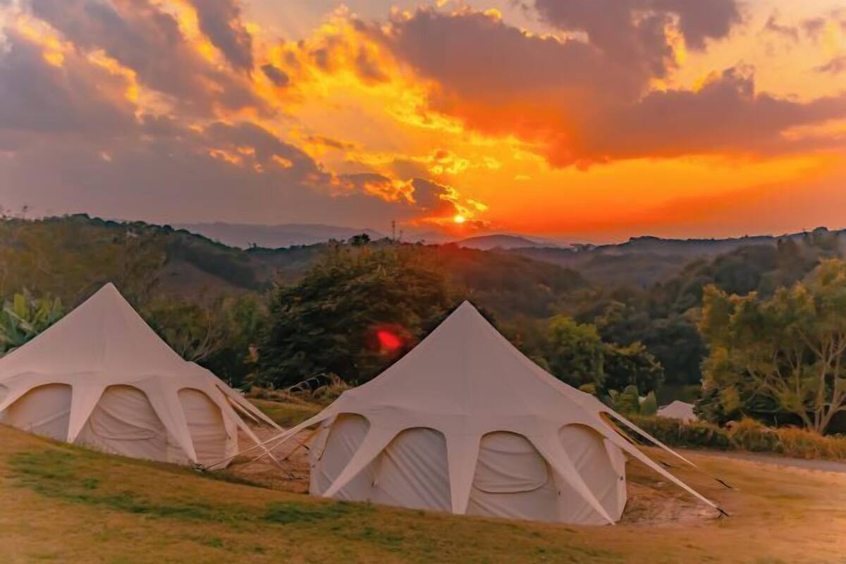 A campsite with two tents, surrounded by hills and trees, during sunset.