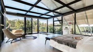 A modern bedroom with a large bed, a chair, and a desk. It features large windows and a view of the outdoors. - Xishuangbanna Visible Zeqi Tent Hotel (Menghai)