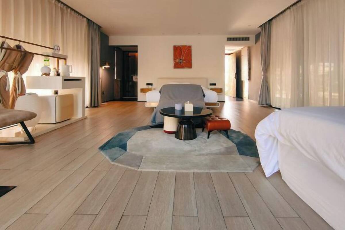 A hotel room with a bed, a sofa, a dining table with candles, and a view of the outside.