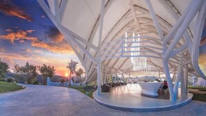 A modern architectural structure with a unique roof design, a central seating area, and a pathway leading to the entrance. - Xishuangbanna Visible Zeqi Tent Hotel (Menghai)