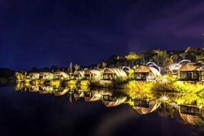 Eine Reihe von kreisrunden, schiffartigen Strukturen mit reflektierenden Oberflächen, gelegen auf ruhigem Gewässer, welches die Strukturen und die umliegende Vegetation spiegelt.