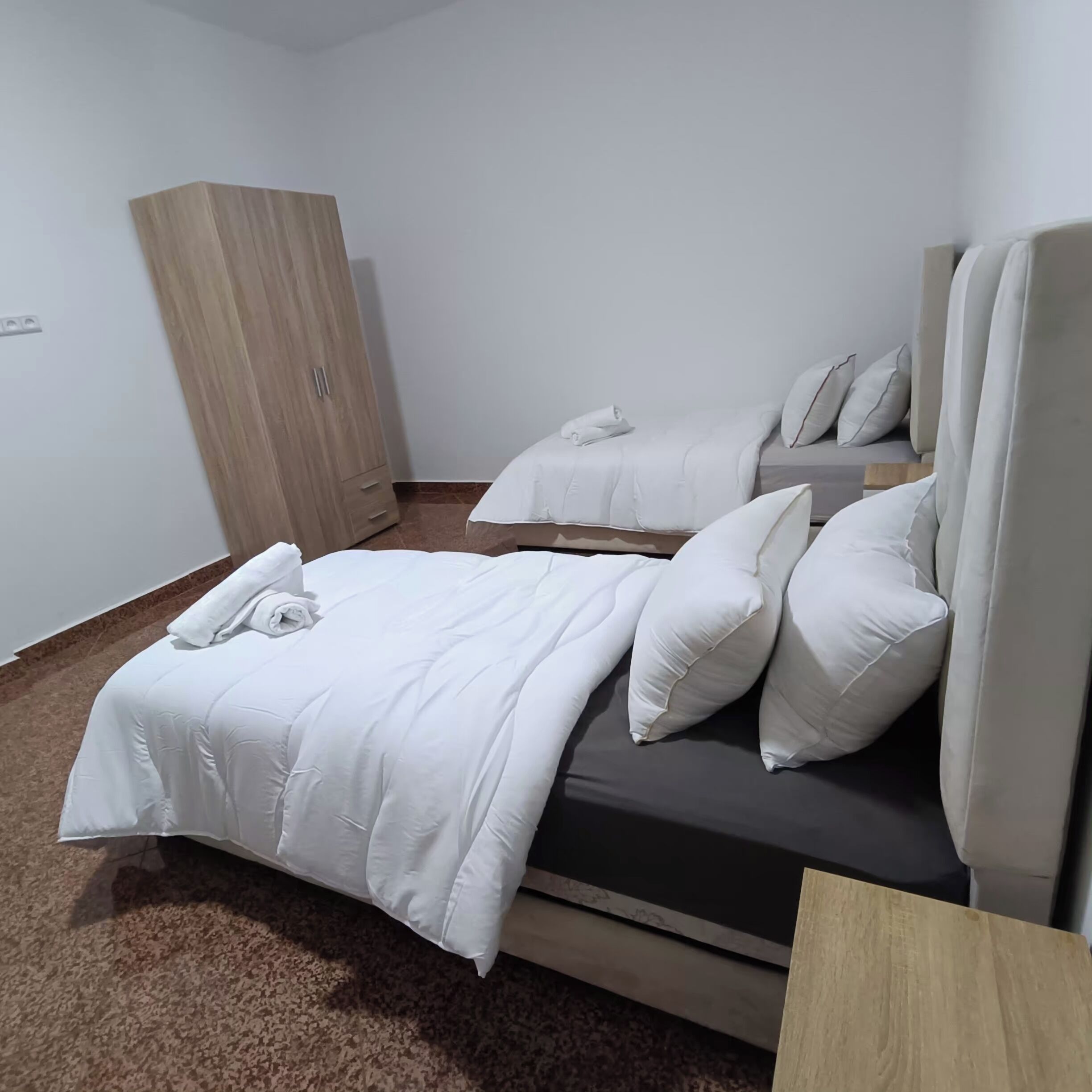 Habitación de hotel con dos camas, un armario y suelo alfombrado.