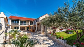 A two-story stone house with a red-tiled roof, a covered patio, and a well-maintained garden with flowering plants and a lawn. - Beautiful home in Benkovac (Benkovac)