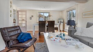 A spacious living room with a leather chair, a grey sofa, a dining area with a table and chairs, and a large window providing natural light. - Lovely home in Pandrup with WiFi (Pandrup)