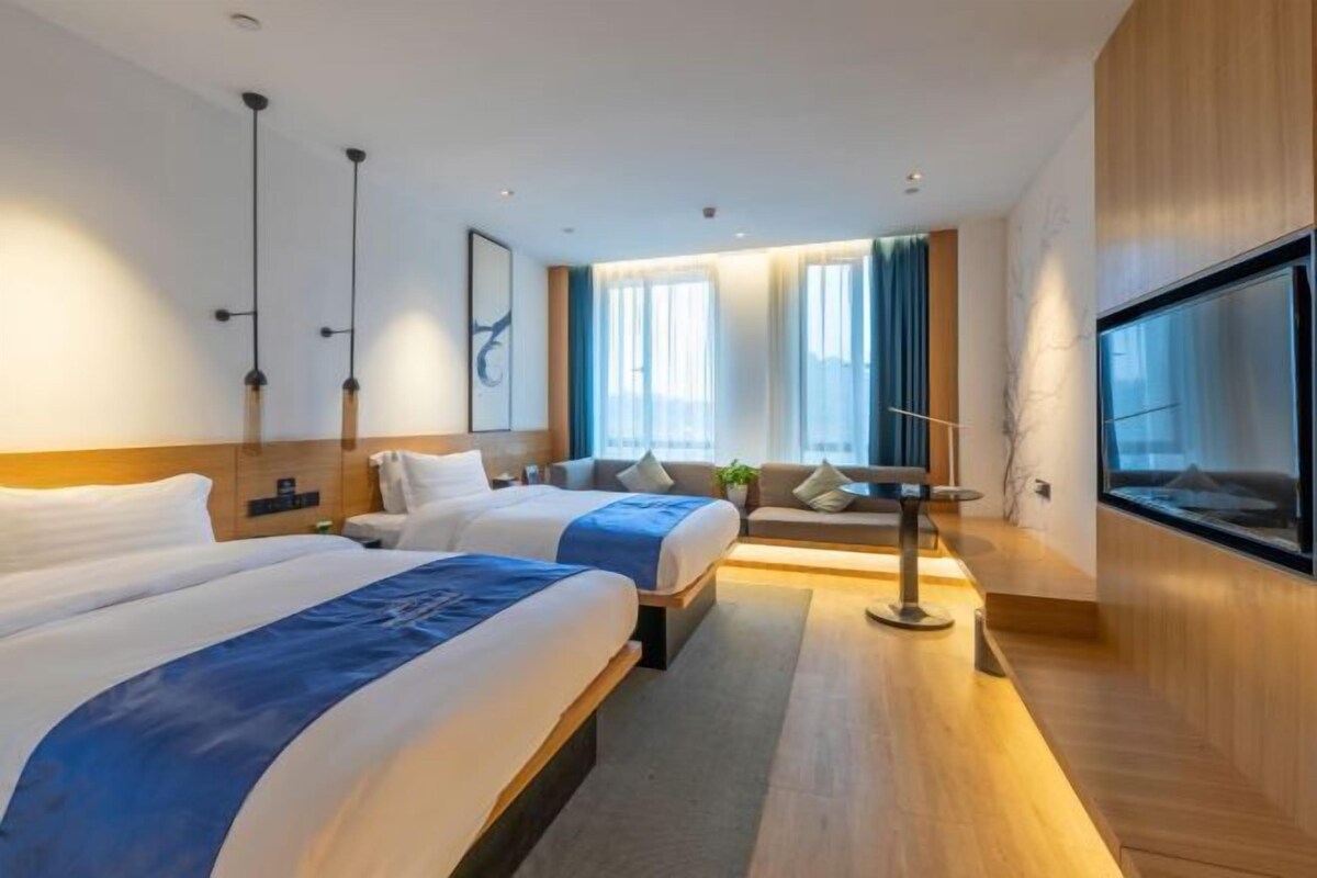 Une chambre d’hôtel moderne avec deux lits, un canapé, une table à manger et de grandes fenêtres.