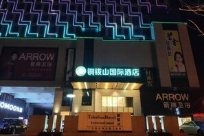 La façade d’un hôtel, ornée d’enseignes lumineuses au néon, notamment les logos « Arrow » et « ToboSanHotel International ».
