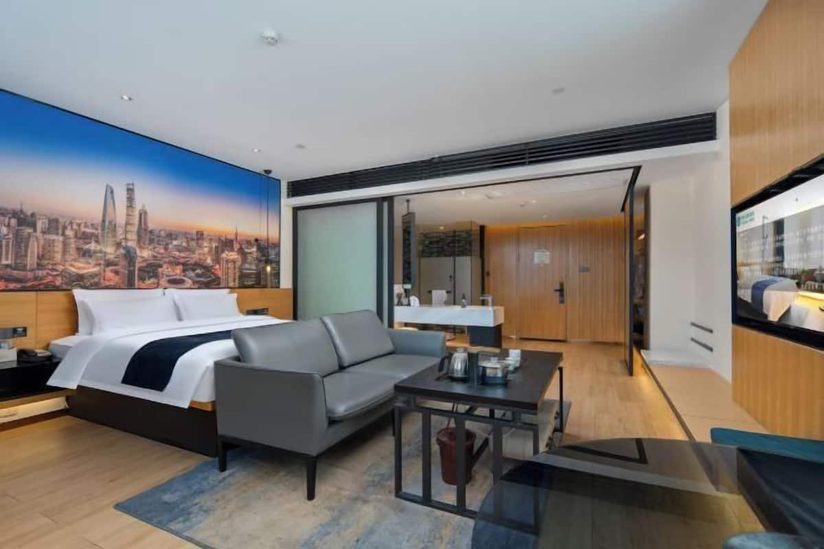 Ein modernes Hotelzimmer mit Stadtbild-Wandgemälde, einem Bett, einer Couch, einem Esstisch und einem separaten Badezimmerbereich.