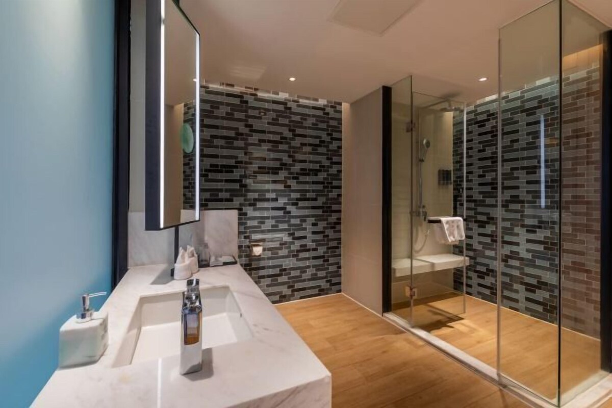 Une salle de bain moderne avec un lavabo en marbre, une cabine de douche en verre et un mur recouvert de mosaïques.