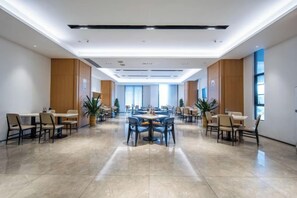 Une salle de conférence d’hôtel spacieuse, dotée de nombreuses tables et chaises, de grandes fenêtres et d’un design moderne au niveau du plafond.