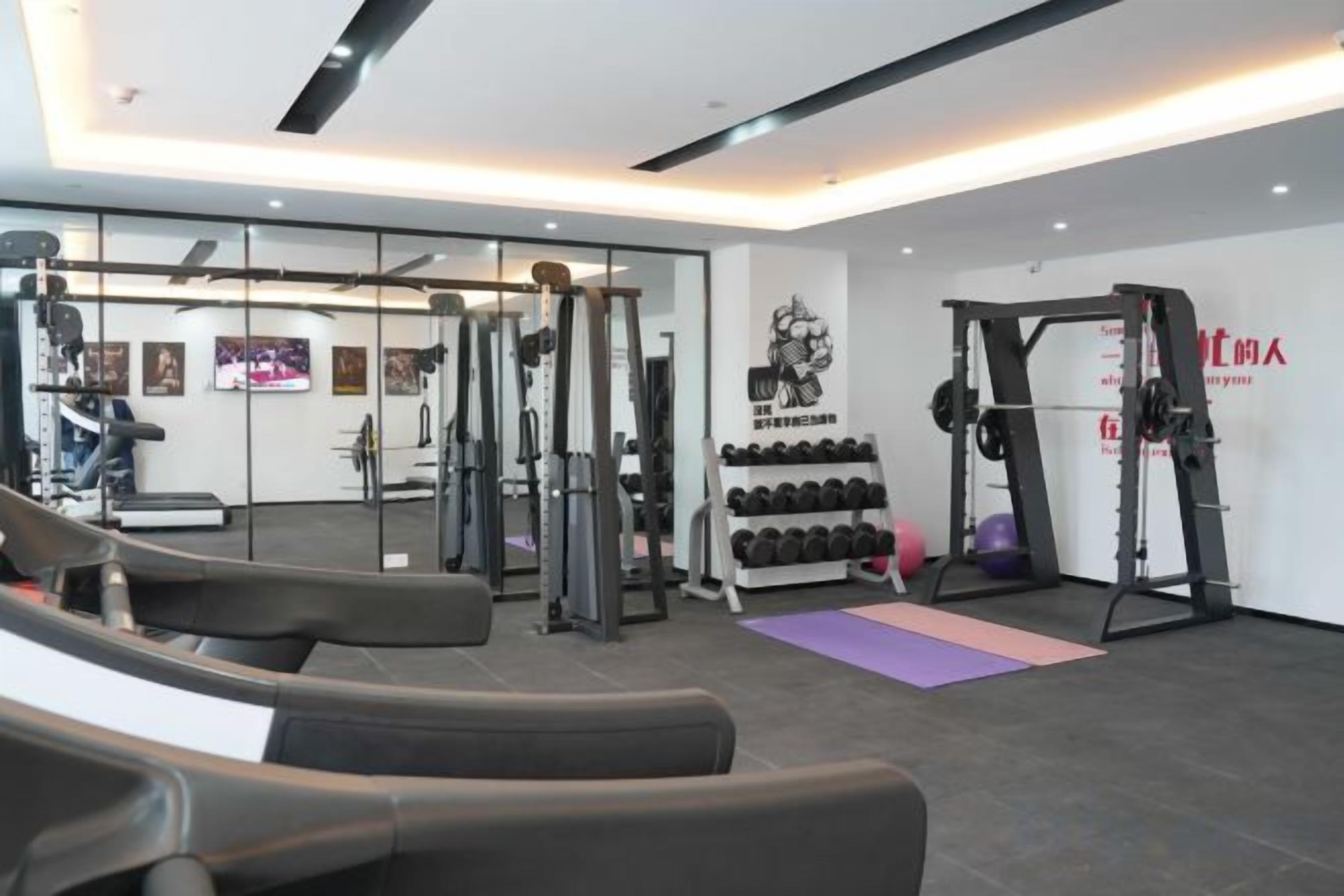 Ein Fitnessraum mit Trainingsgeräten, einem Gewichtständer und einer Yogamatte.
