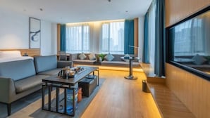 Ein modernes Hotelzimmer mit einer Couch, einem Esstisch, einer Lampe und großen Fenstern mit Vorhängen.