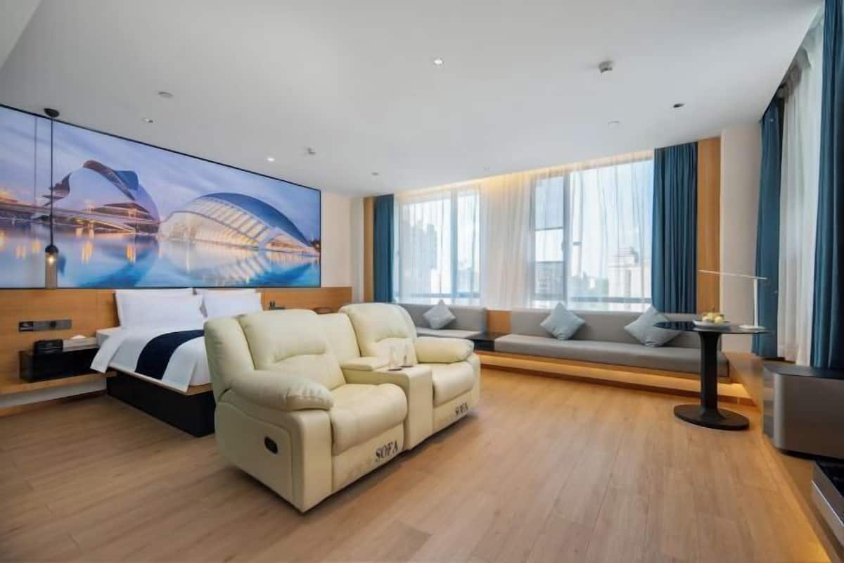 Ein modernes Hotelzimmer mit einer Couch, einem Bett, einem kleinen Tisch und einem großen Fenster mit Vorhängen.
