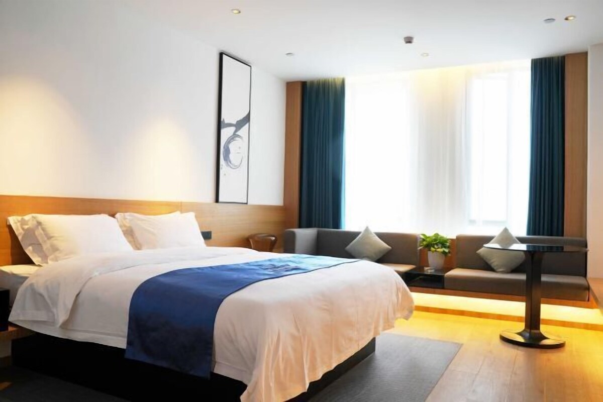 Une chambre d’hôtel moderne avec un grand lit, un canapé, une petite table et une fenêtre avec des rideaux.