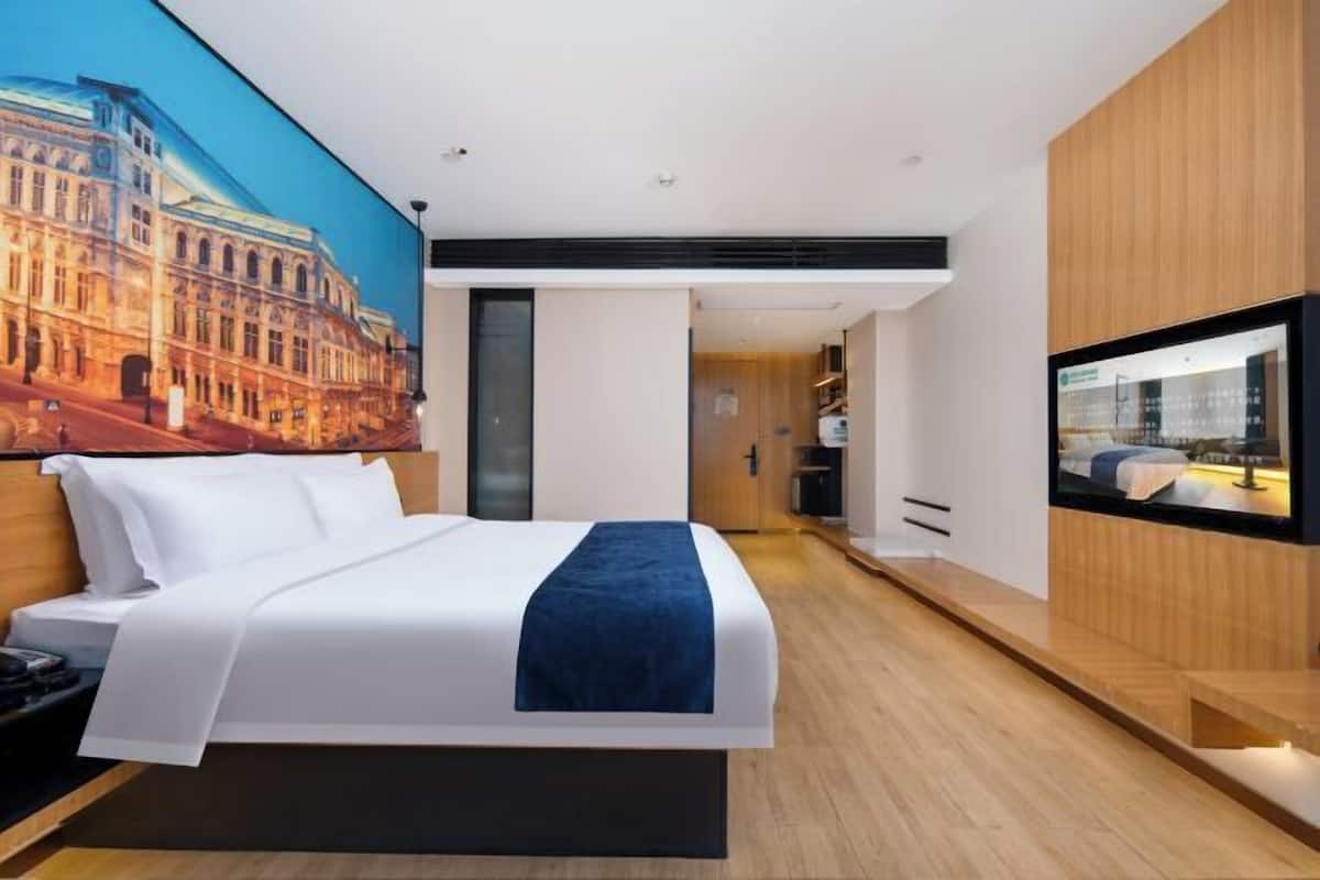 Ein modernes Hotelzimmer mit einem großen Bett, einem Flachbildfernseher und einem Wandbild mit Stadtansicht.
