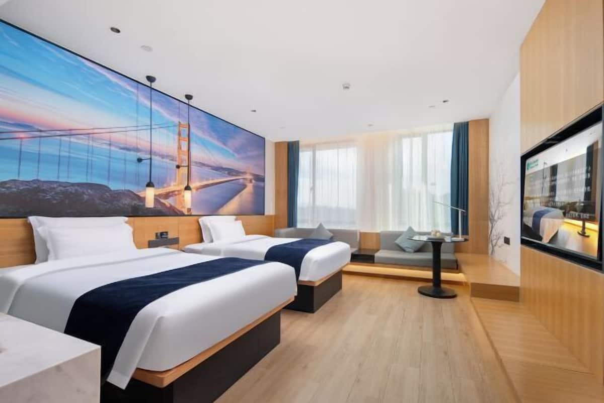 Ein Hotelzimmer mit zwei Betten, einem großen Fenster mit Vorhängen, einem Flachbildfernseher und einem Gemälde einer Brücke.