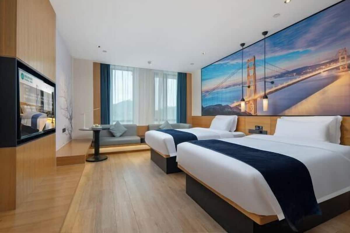 Ein Hotelzimmer mit zwei Betten, einem Sofa, einem Fernseher und einem großen Gemälde einer Brücke.