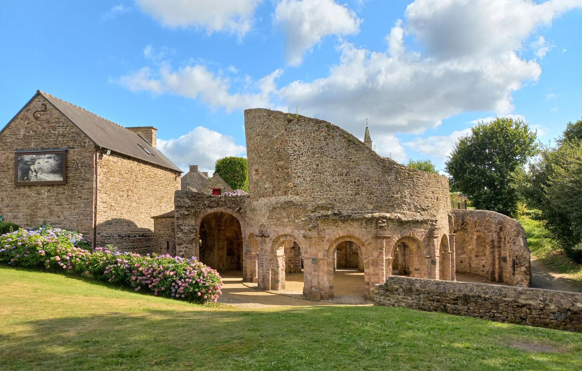 Un ancien bâtiment en pierre, doté d’une grande entrée en arc de cercle et d’un bâtiment plus petit, orné d’une image sur le mur.