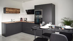 Une cuisine moderne avec des meubles de couleur sombre, un plan de travail en bois et un coin repas aménagé pour quatre personnes, avec une table dressée pour le repas.