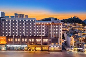 A multi-story hotel with a modern facade, located in an urban setting with a view of the cityscape and a hill in the background. - The Sleep Ziihome Hotel (Guiyang)
