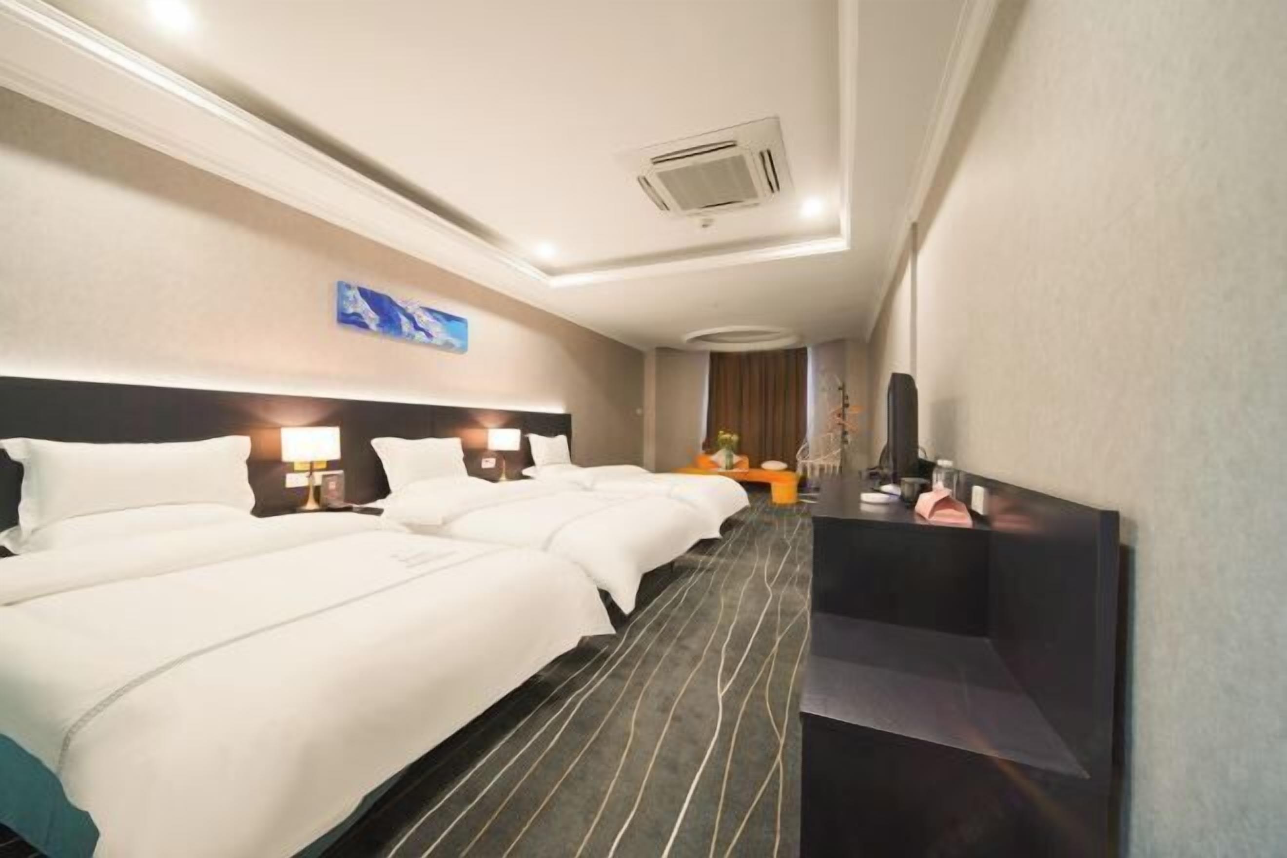 Une chambre d’hôtel avec deux lits, un bureau, un miroir et un climatiseur fixé au mur.