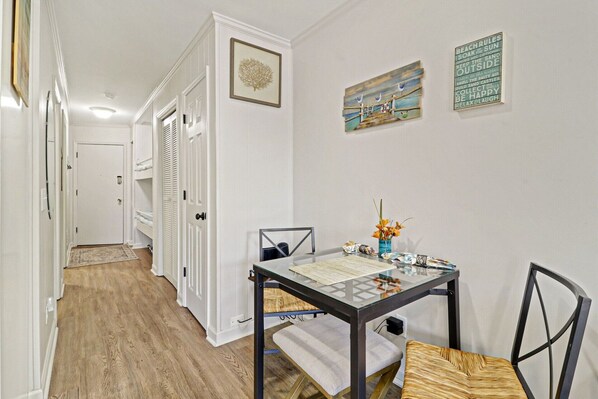 A hallway with white doors, a dining area with a glass table and chairs, and wall art.