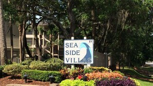 A sign for 'SEA SIDE VILLAS' with a number 23, surrounded by landscaped garden beds and trees. - Family Beachfront Retreat: Walk to Coligny Plaza with Side Ocean Views (Hilton Head Island)