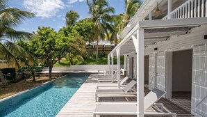 Uma área à beira da piscina com espreguiçadeiras, um deck de madeira e palmeiras.