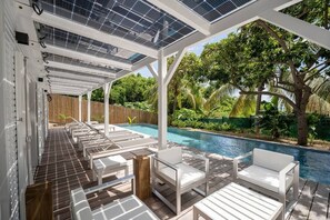 Un espace extérieur abrité comprenant une piscine, des chaises longues blanches et des panneaux solaires sur le toit.