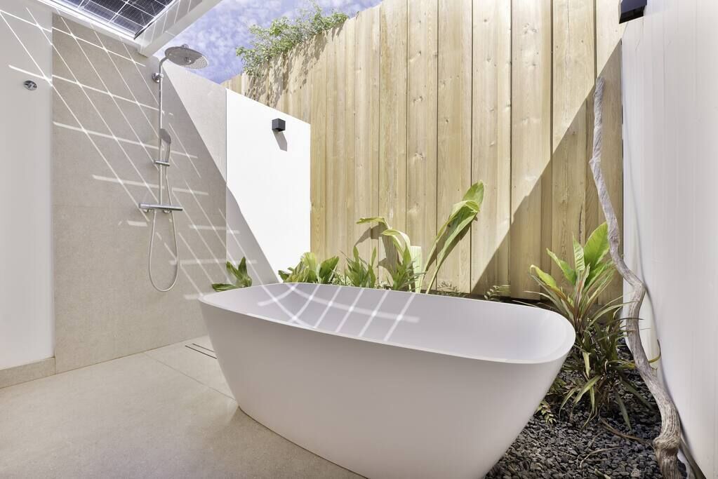 Una bañera exterior moderna con un cerco de madera y plantas al fondo.