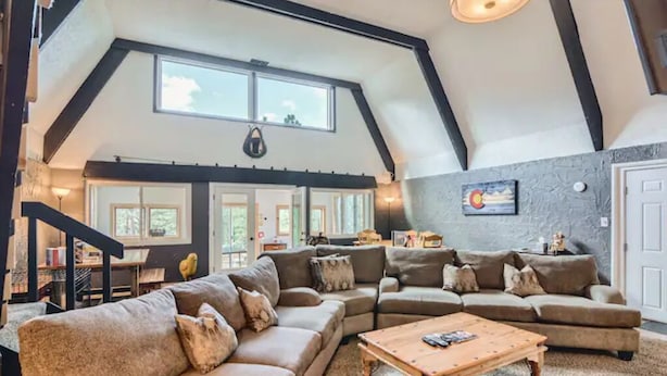 A spacious living room with a high ceiling, large windows, and a cozy seating area. - Cabin in the Woods with Hot Tub, Incredible Views, Fireplace, Foosball, Fire Pit (Green Mountain Falls)