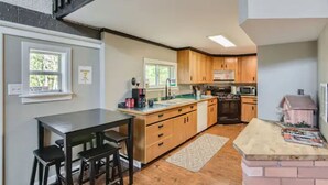 A modern kitchen with wooden cabinets, a central island, and a dining area with a table and chairs. - Cabin in the Woods with Hot Tub, Incredible Views, Fireplace, Foosball, Fire Pit (Green Mountain Falls)