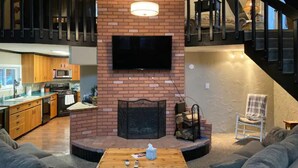 A modern living room with a fireplace, a television mounted on the wall, and a dining area with a table and chairs. - Cabin in the Woods with Hot Tub, Incredible Views, Fireplace, Foosball, Fire Pit (Green Mountain Falls)