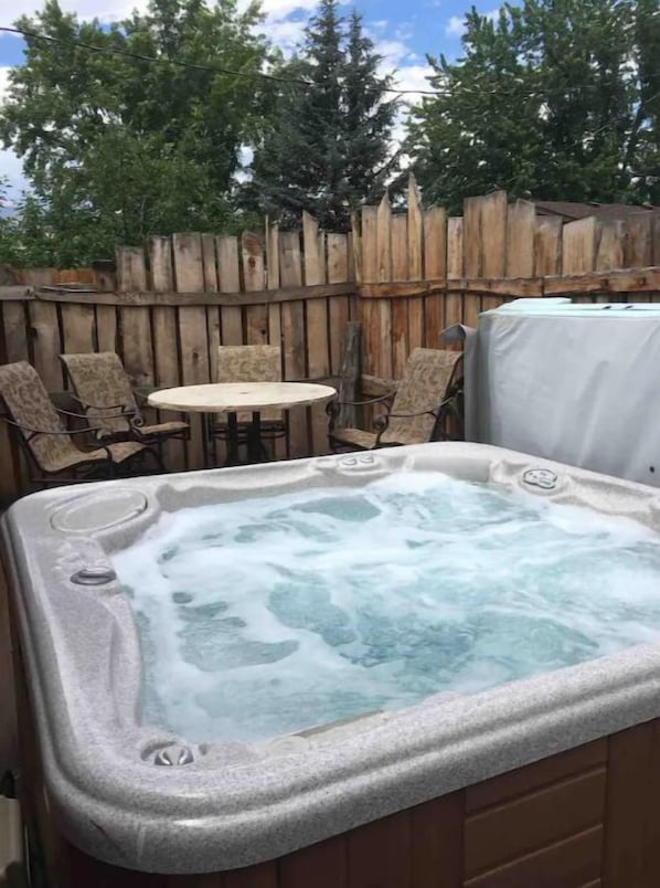 A hot tub with a wooden fence and chairs in the background.