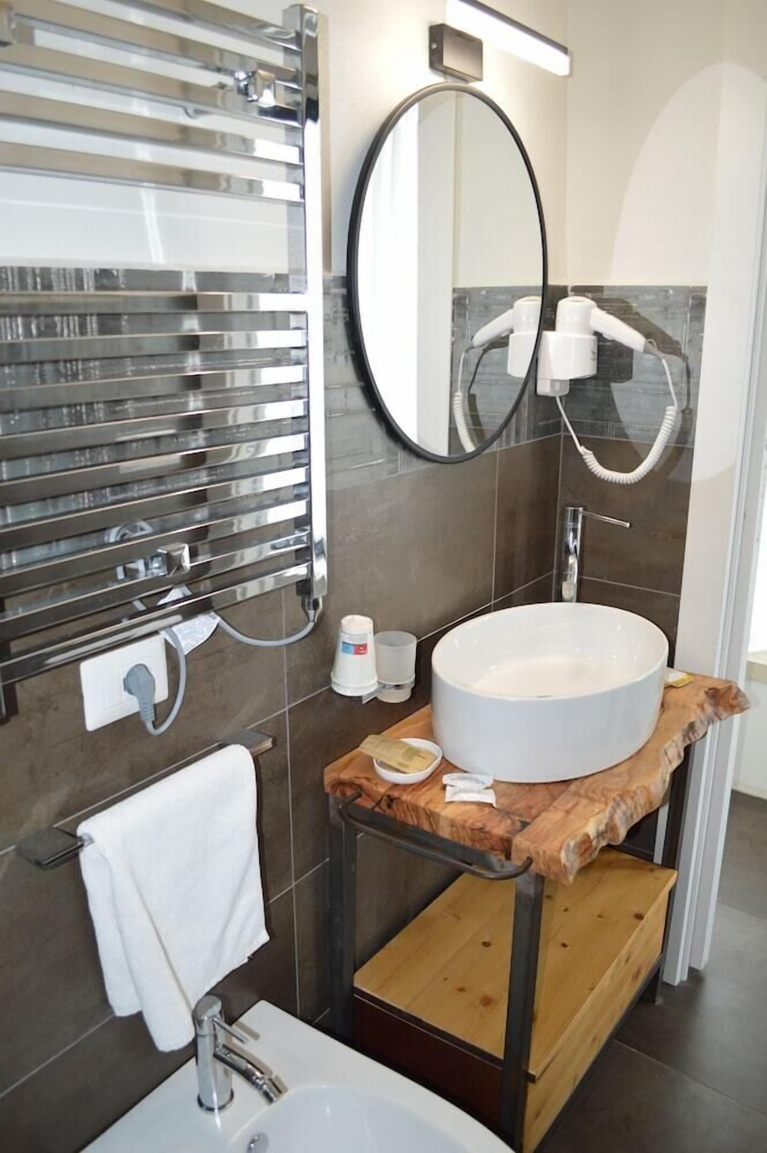 A modern bathroom with a round sink, a mirror, a towel rack, and a shower area.