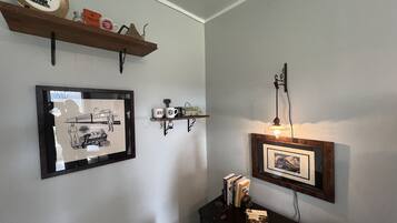 Una habitación con un cuadro de un tren, una estantería con tazas y una lámpara fijada en la pared.