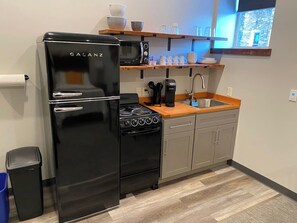 Eine kompakte Küche mit einem schwarzen Galanz-Kühlschrank, einer Mikrowelle, einer Kaffeemaschine und einem Spülbecken.