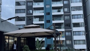 A modern multi-story building with balconies, a covered outdoor seating area with tables and chairs, and potted plants. - Indesign Studio  (Syokimau)
