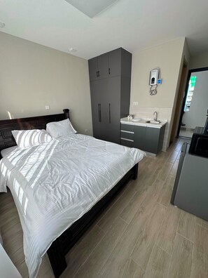 A bedroom with a large bed, a wardrobe, a sink, and a refrigerator.