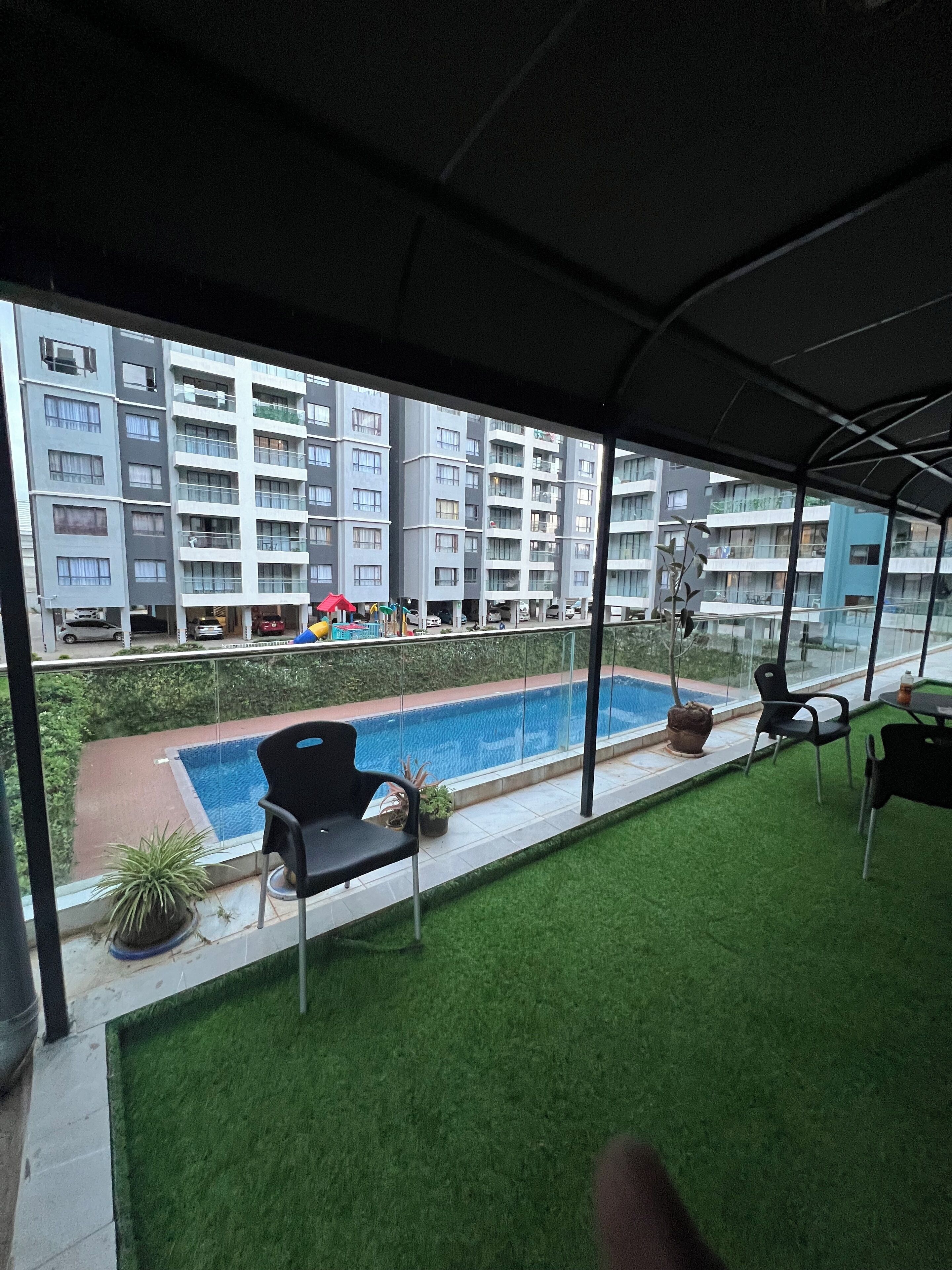 En balkon med udsigt over en swimmingpool, krukker med planter og udendørs møbler.