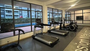 A gym with treadmills and stationary bikes, large windows with a view of buildings, and a sign reading "Indesit Mobi". - Indesign Studio  (Syokimau)