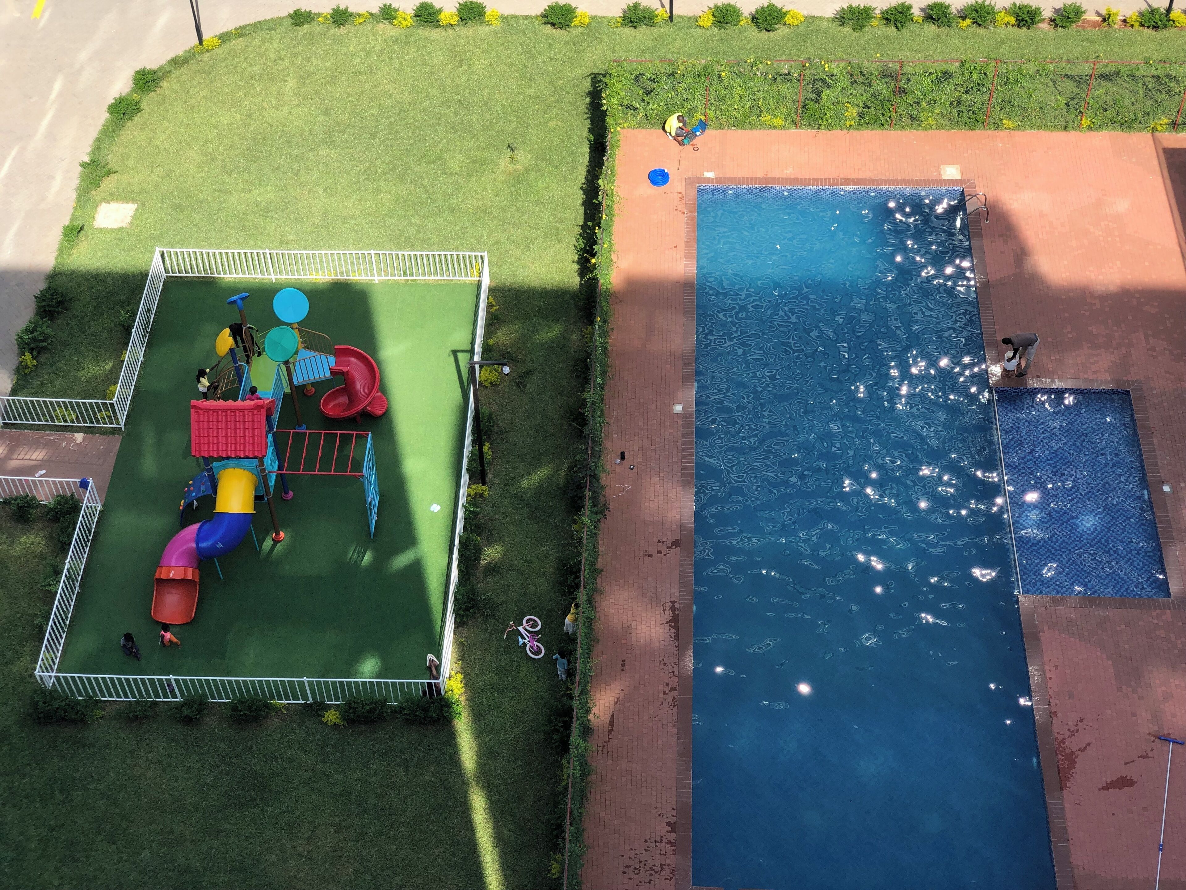 An aerial view of a playground with a slide and climbing structures, adjacent to a swimming pool with a tiled deck.